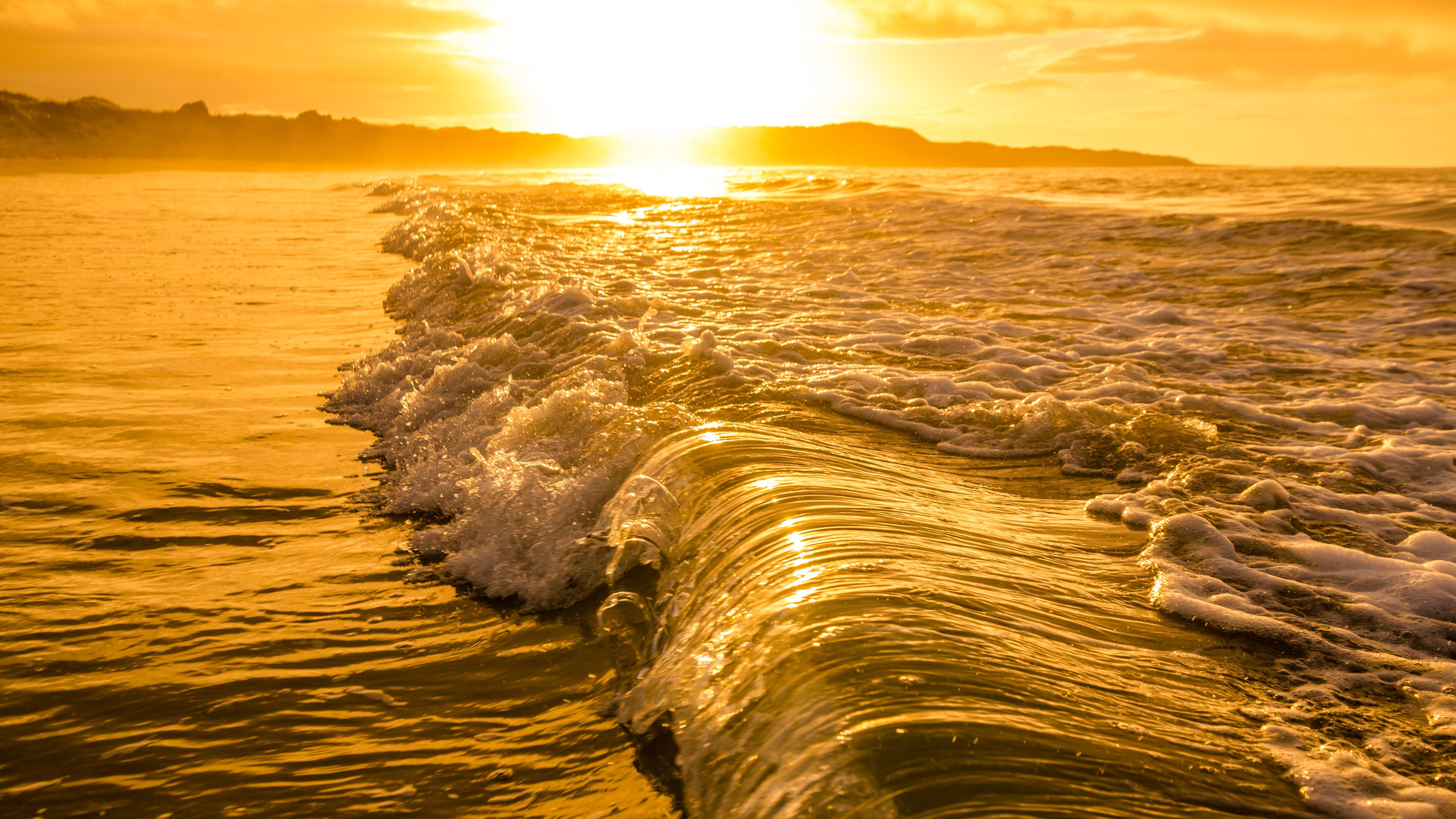 Foamy waves rolling onto a beach under a golden sunrise.