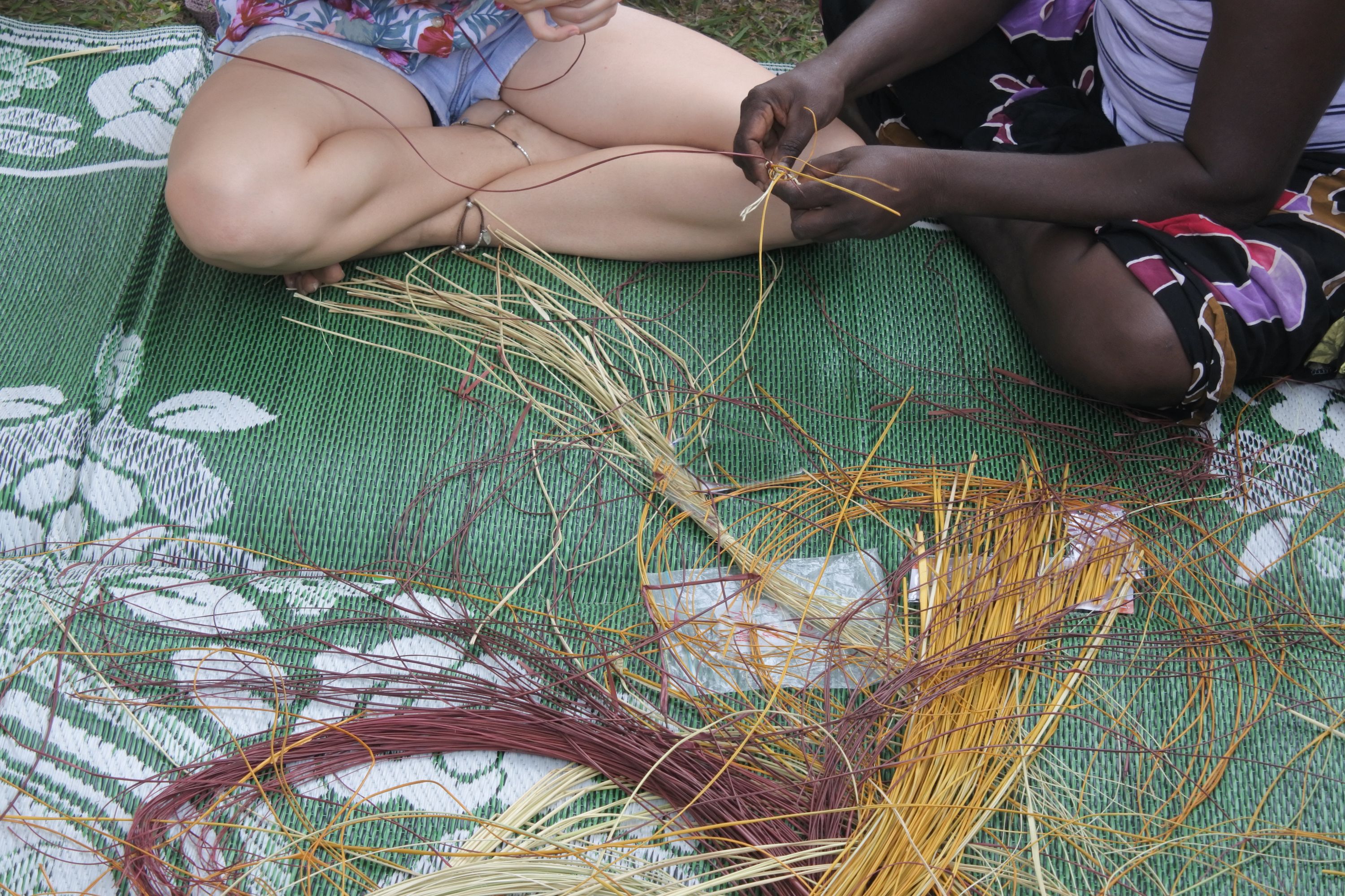 Aboriginal woman teaching a tourist Aboriginal basket weaving technique. Photographer_Rafael Ben Ari. Source_Getty Images. Used under Licence Aboriginal woman teaches tourist how to weave on a green mat, faces not showing