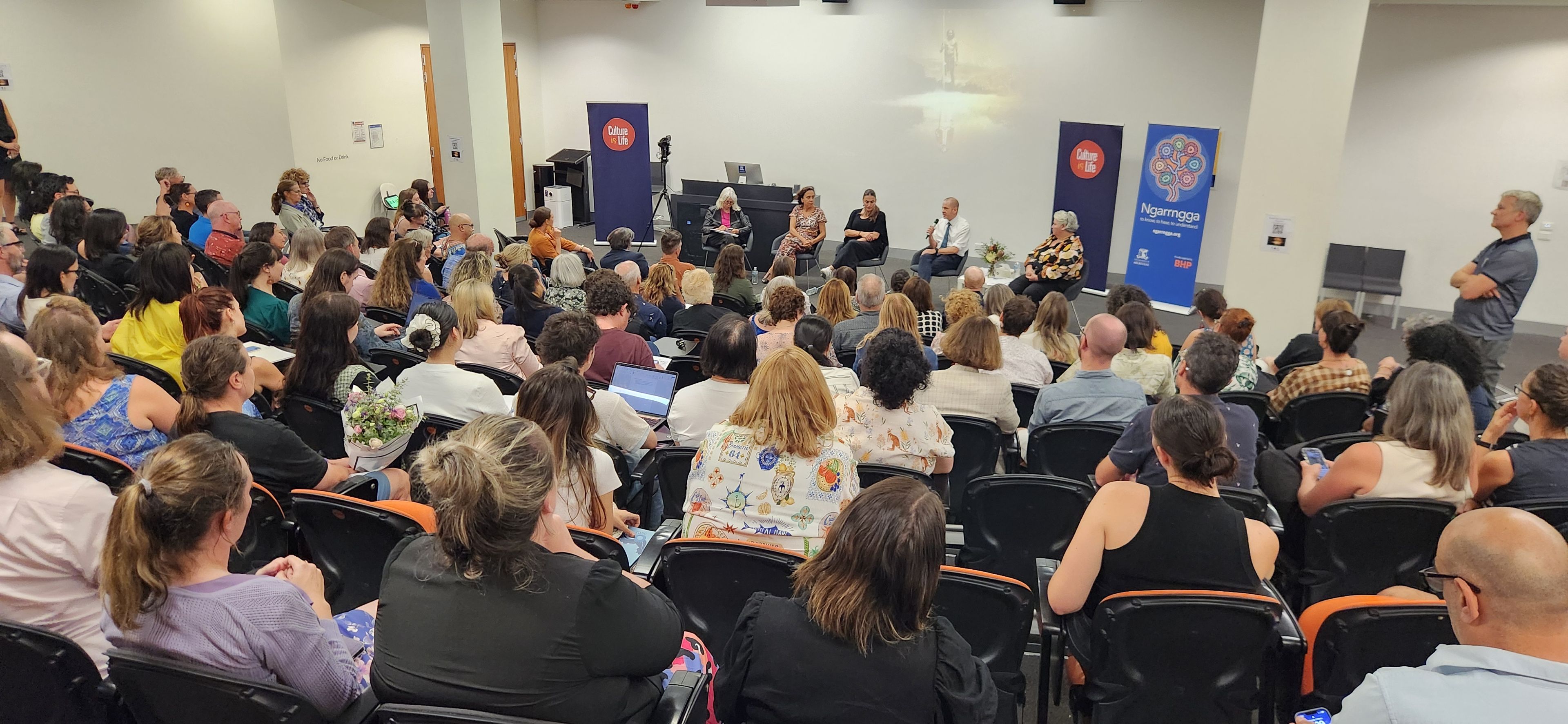 Image from the Teaching the Australian Wars Panel Lecture theatre full of educators watching Teaching the Australian Wars Panel event, with Rachel Perkins, Marcia Langton, Belinda Duarte, Bill Lewis and Melitta Hogarth speaking